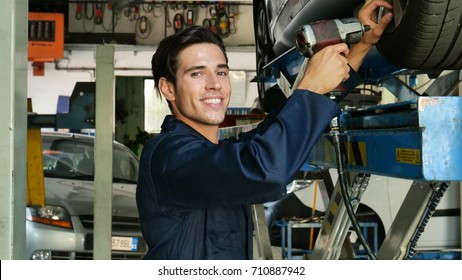 Portrait of a mechanic in a garage who while smashing machine tires smiles. Concept of: assistance, warranty, machines, insurance and professionalism and maintenance. - Powered by Shutterstock