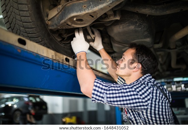 Portrait of mechanic\
repairing a lifted car