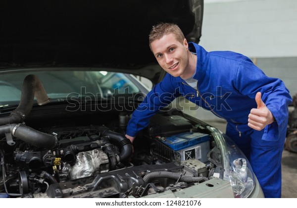 Portrait\
of mechanic under car bonnet gesturing thumbs\
up