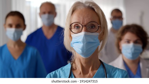 Portrait Of Medical Staff In Uniform And Protective Mask Looking At Camera. Team Of Professional Medicine Workers In Safety Mask Posing At Camera Together In Hospital