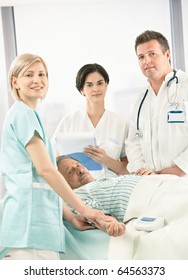 Portrait Of Medical Team With Old Patient In Hospital, Smiling Nurse Measuring Blood Pressure.