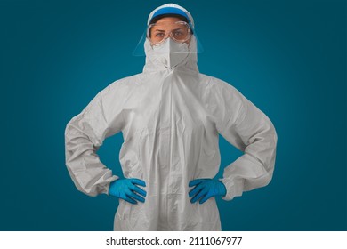 Portrait Of A Medical Worker Wearing Biohazard Protective Suit Or PPE, Goggles, Face Shield, White N95 Mask And Gloves Isolated On Blue Background. Protection From Infectious Disease, Disease.