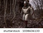 Portrait of Medieval Infantryman running along an old trail with sward, shield and helm. Image ideal for book covers dedicated to medieval battles, stories and myths.