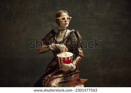 Portrait of medieval princess in vintage dress and 3D movie glasses, eating popcorn against dark green background. Concept of history, renaissance art remake, comparison of eras, modern leisure