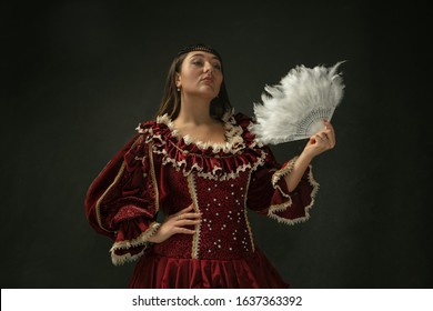 Portrait Of Medieval Young Woman In Red Vintage Clothing Posing With Fluffy Fur On Dark Background. Female Model As A Duchess, Royal Person. Concept Of Comparison Of Eras, Modern, Fashion, Beauty.