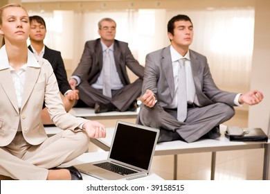 Portrait of meditating business people sitting on desks with their legs crossed in office - Powered by Shutterstock