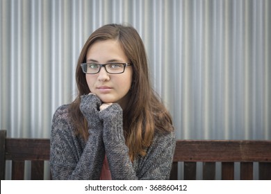 Portrait Of Melancholy Young Girl With Glasses Sitting On Bench.