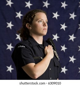 Portrait of mid adult Caucasian policewoman pledging allegiance with American flag as backdrop.
