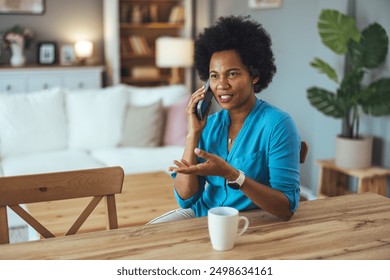 Portrait of mid adult woman sitting on the chair in the living room and talking on the phone. African American woman making a phone call. African American woman having a conversation on her cell phone - Powered by Shutterstock