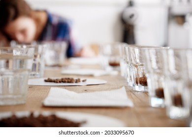 Portrait Of Mid Age Woman In Selective Focus Smelling Coffee Beans In Cup At Coffee Cupping Process. There Are Rows Of Cups With Coffee Beans For A Test On Wooden Table. Barista Examine