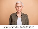 Portrait of middle age blond short hair business lady wearing khaki shirt confident posing non emotional isolated on beige color background