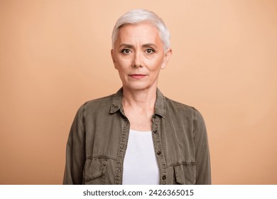 Portrait of middle age blond short hair business lady wearing khaki shirt confident posing non emotional isolated on beige color background