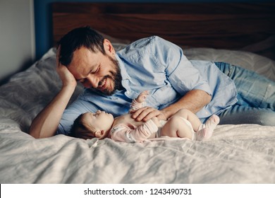 Portrait Of Middle Age Caucasian Father Talking To Newborn Baby Son Daughter. Male Man Parent Smiling To Child On Bed In Bedroom At Home. Authentic Lifestyle Real Candid Moment. 