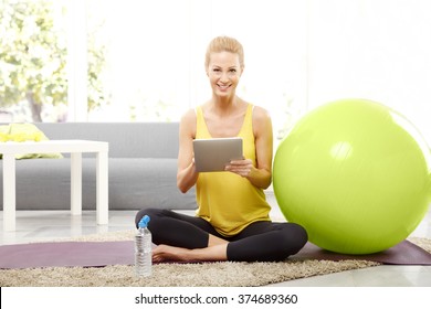 Portrait Of Middle Age Woman Sitting At Home In Living Room After Morning Workout And Using Digital Tablet. 