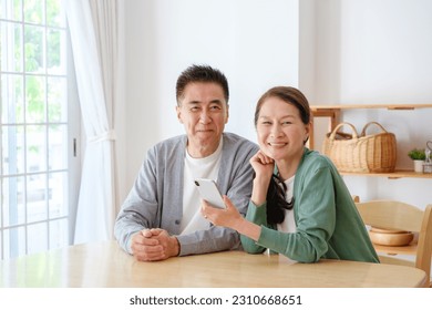 portrait of middle aged asian couple using smartphone in living room - Powered by Shutterstock