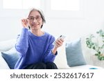 portrait of middle aged asian woman using smartphone with reading glasses in living room