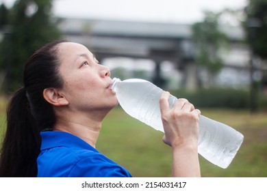 Portrait Of Middle Aged Asian Woman Drinking Water After Running Outdoors.