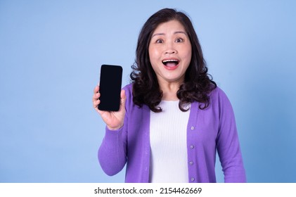 Portrait Of Middle Aged Asian Woman Using Smartphone On Blue Background