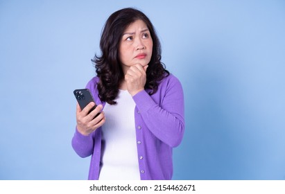 Portrait of middle aged Asian woman using smartphone on blue background - Powered by Shutterstock