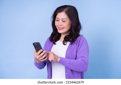 Portrait of middle aged Asian woman using smartphone on blue background - Powered by Shutterstock