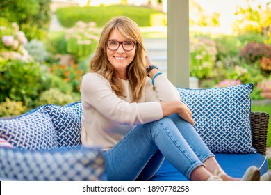 Portrait of middle aged attractive woman looking at camera and smiling while relaxing at the balcony at home. 