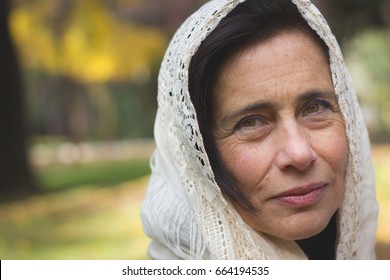 Portrait Of Middle Aged Beautiful Lady With White Shawl Over Head And Thoughtful Expression Outdoors. Young Looking Woman With White Veil Covering Head. Arab, Muslim Look