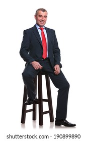 Portrait Of A Middle Aged Business Man Sitting On A High Stool And Smiling For The Camera. Isolated On A White Background