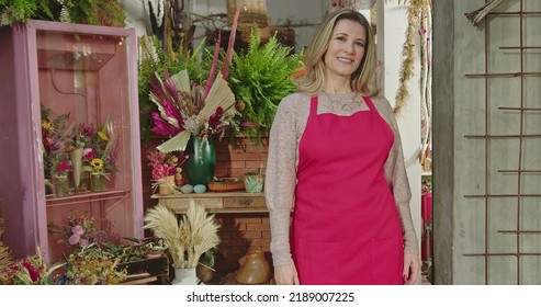 Portrait Of A Middle Aged Businesswoman Entrepreneur Owner Of Local Small Business Shop Wearing Apron Looking At Camera. Woman Owner Of Flower Shop Standing In Business Storefront