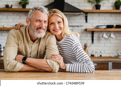 Portrait of middle aged couple hugging while standing together in kitchen at home - Shutterstock ID 1743489539