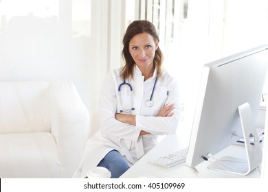 Portrait Of Middle Aged Female Doctor Sitting At Private Clinic In Exam Room.