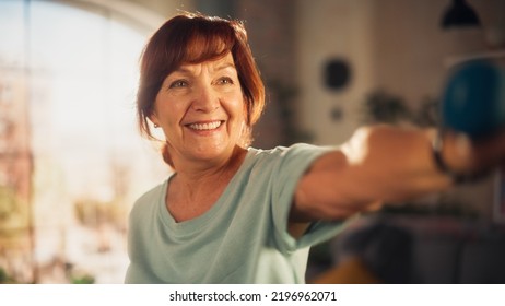 Portrait Of A Middle Aged Female Exercising And Training At Home In The Morning. Elderly Female Strengthening Arm Muscles With Dumbbell Workout In Bright Apartment Living Room. Wellness And Fitness.