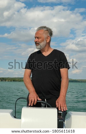 Portrait of a middle aged handsome man with grey hair on his boat on the lake