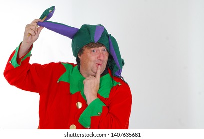 A portrait of a middle aged man dressed as a jester in a foolish pose and with a silly expression against a white background