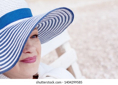 Portrait Middle Aged Mature Woman Posing On The Beach In The Sea. Wearing Grey Dress, Straw Hat And Bag