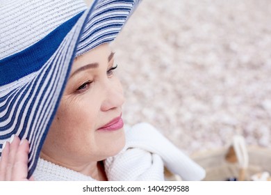 Portrait Middle Aged Mature Woman Posing On The Beach In The Sea. Wearing Grey Dress, Straw Hat And Bag