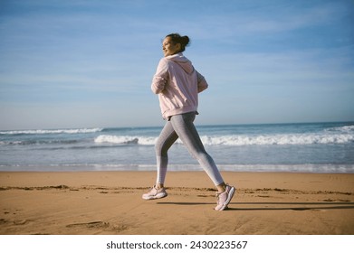 Portrait of middle aged multi ethnic happy active sportswoman running along the Atlantic beach. Healthy fitness woman jogging outdoors. Sports and healthy lifestyle concept. Full length side portrait - Powered by Shutterstock