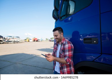 Portrait Of Middle Aged Professional Trucker Driver Standing By His Truck At Truck Stop Using Tablet Computer.