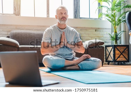 Portrait of middle aged sport man doing yoga and fitness at home using laptop