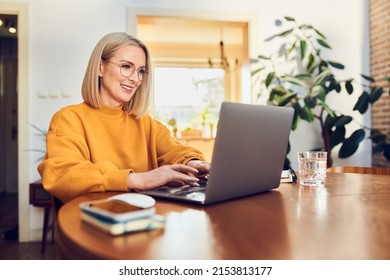 Portrait of middle aged woman sitting at dinning with laptop working at home - Powered by Shutterstock