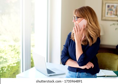 Portrait Of Middle Aged Woman Using Mobile Phone And Making A Call While Working From Home. Home Office.