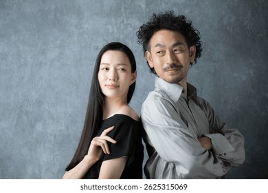 Retrato de una pareja intermedia, un hombre y una mujer japoneses de moda, de pie frente a una bolsa gris.