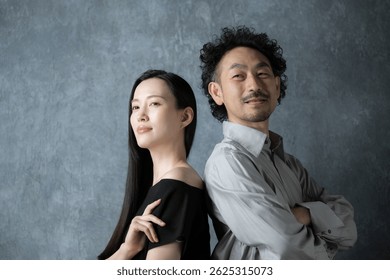 Retrato de una pareja intermedia, un hombre y una mujer japoneses de moda, de pie frente a una bolsa gris. Mirando hacia arriba.
