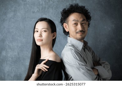 Retrato de una pareja intermedia, un hombre y una mujer japoneses de moda, de pie frente a una bolsa gris. Mirando a la cámara.