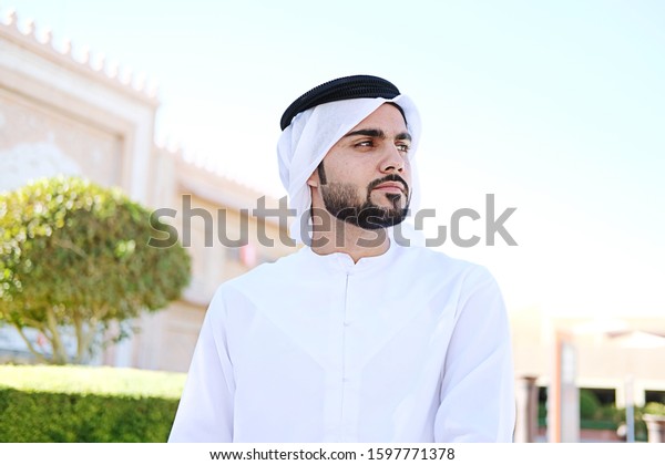 Portrait of Middle Eastern Arab man looking on\
his side on Kandura. Emirati Arabian businessman wearing dish dasha\
with copy space and sky\
background