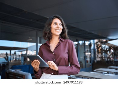 Portrait of middle eastern businesswoman using tablet pc app standing at office business building outdoors. Smiling indian or latin hispanic woman holding digital computer, looking aside. Copy space - Powered by Shutterstock