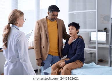 Portrait of Middle Eastern father and son visiting doctor in clinic with young boy explaining symptoms and pointing at throat - Powered by Shutterstock