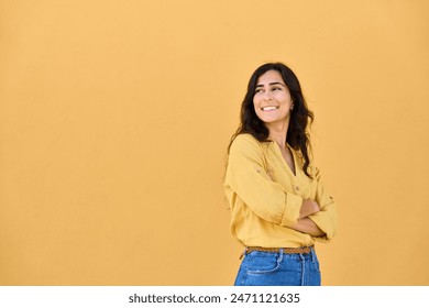 Portrait of middle eastern Israel girl student standing with crossed arms isolated on yellow background. Smiling young Arabian Indian woman, businesswoman, business lady looking aside at copy space - Powered by Shutterstock