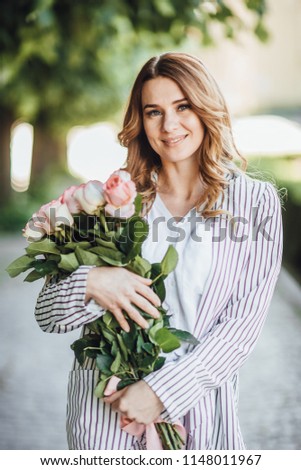 Portrait of a middle-aged blonde woman in casual clothes in the street with a bouquet of roses. Blurred back background.