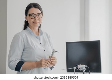 Portrait of middle-aged female otolaryngologist specialist with otoscope in hands looking in camera in modern clinic hospital. Eye nose illnesses treatment. - Powered by Shutterstock