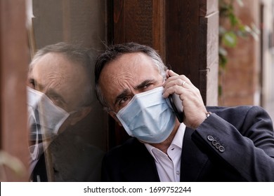 Portrait Of Middle-aged Man In Jacket With Protective Face Mask, Reflected In A Glass Calling On A Cell Phone